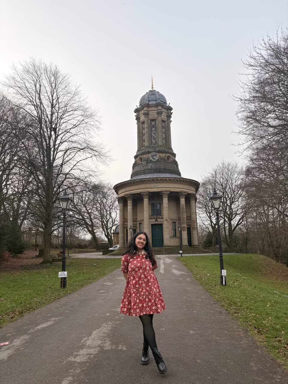 Ananya on a tree-lined road in front of a stone building and clock tower